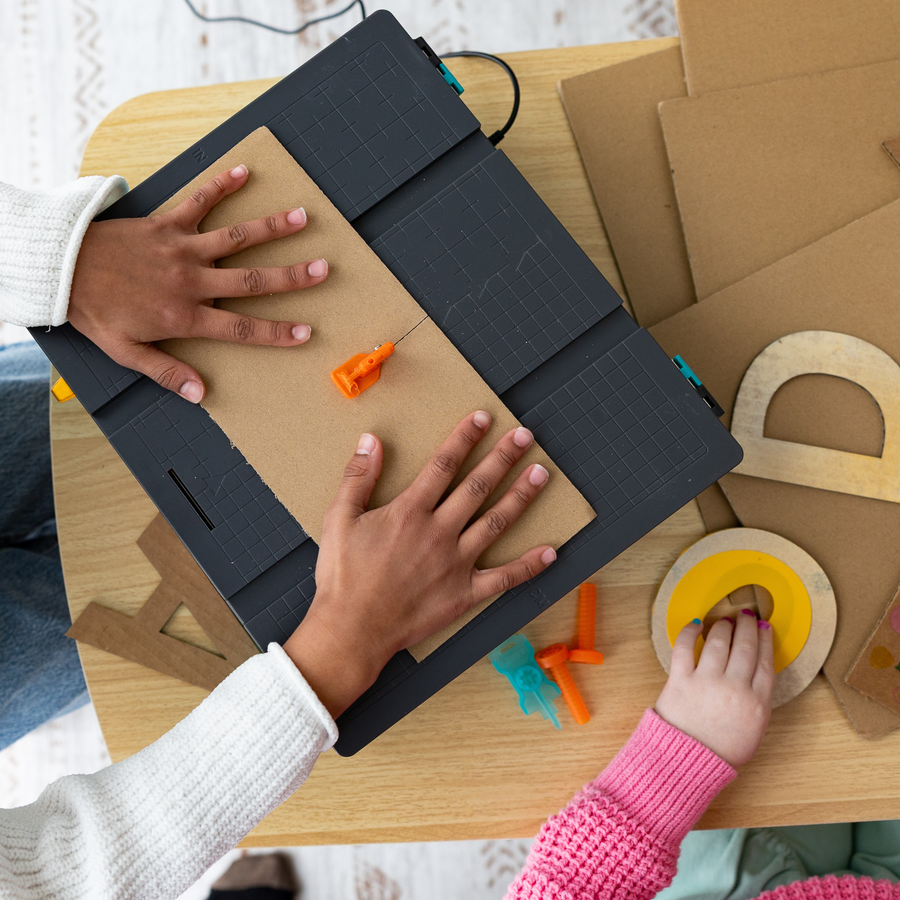 Kids guiding cardboard across the Swift Saw